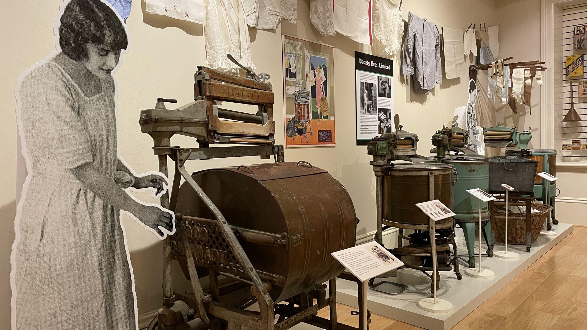 1920s electric wringer washing machines on exhibit with laundry hanging above.