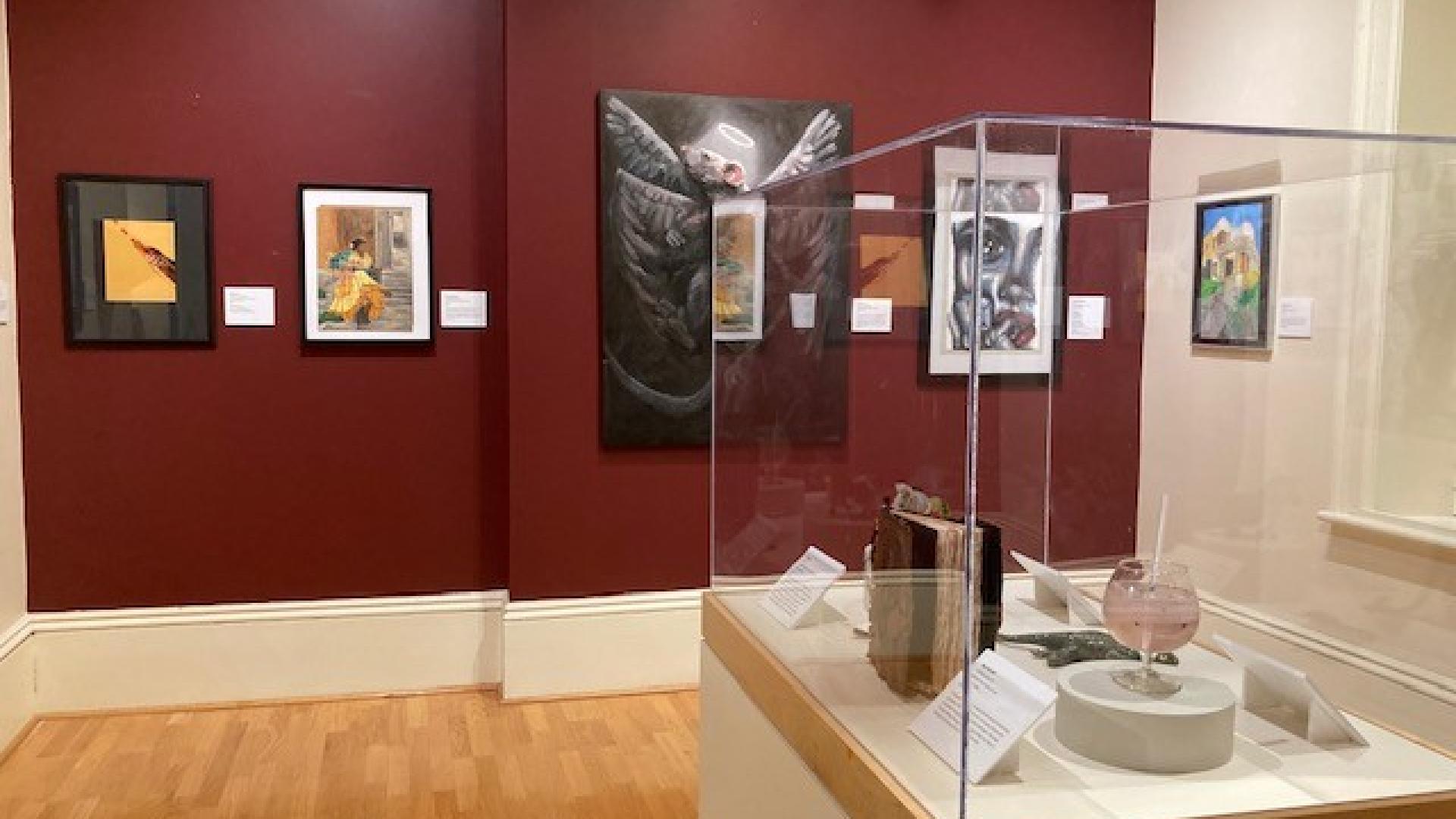 Art pieces hanging on a red wall with a display case in the foreground.