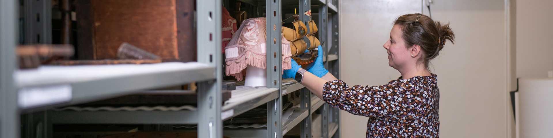 Archivist wearing blue latex gloves places an artifact on a metal shelf
